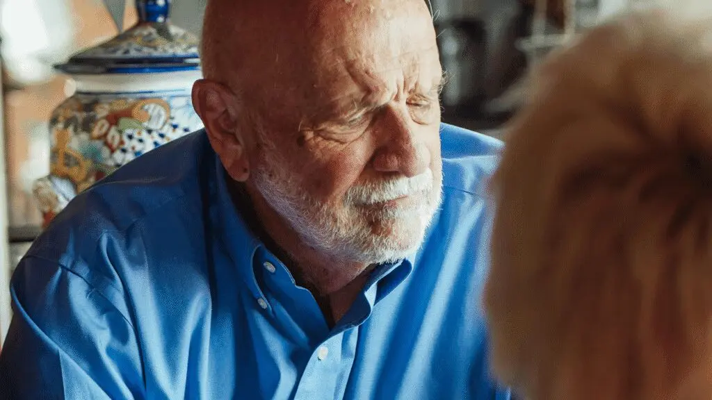 A close-up of a thoughtful-looking senior man with a white beard, wearing a blue shirt, listening intently. (This image can represent someone considering their benefits or financial future).