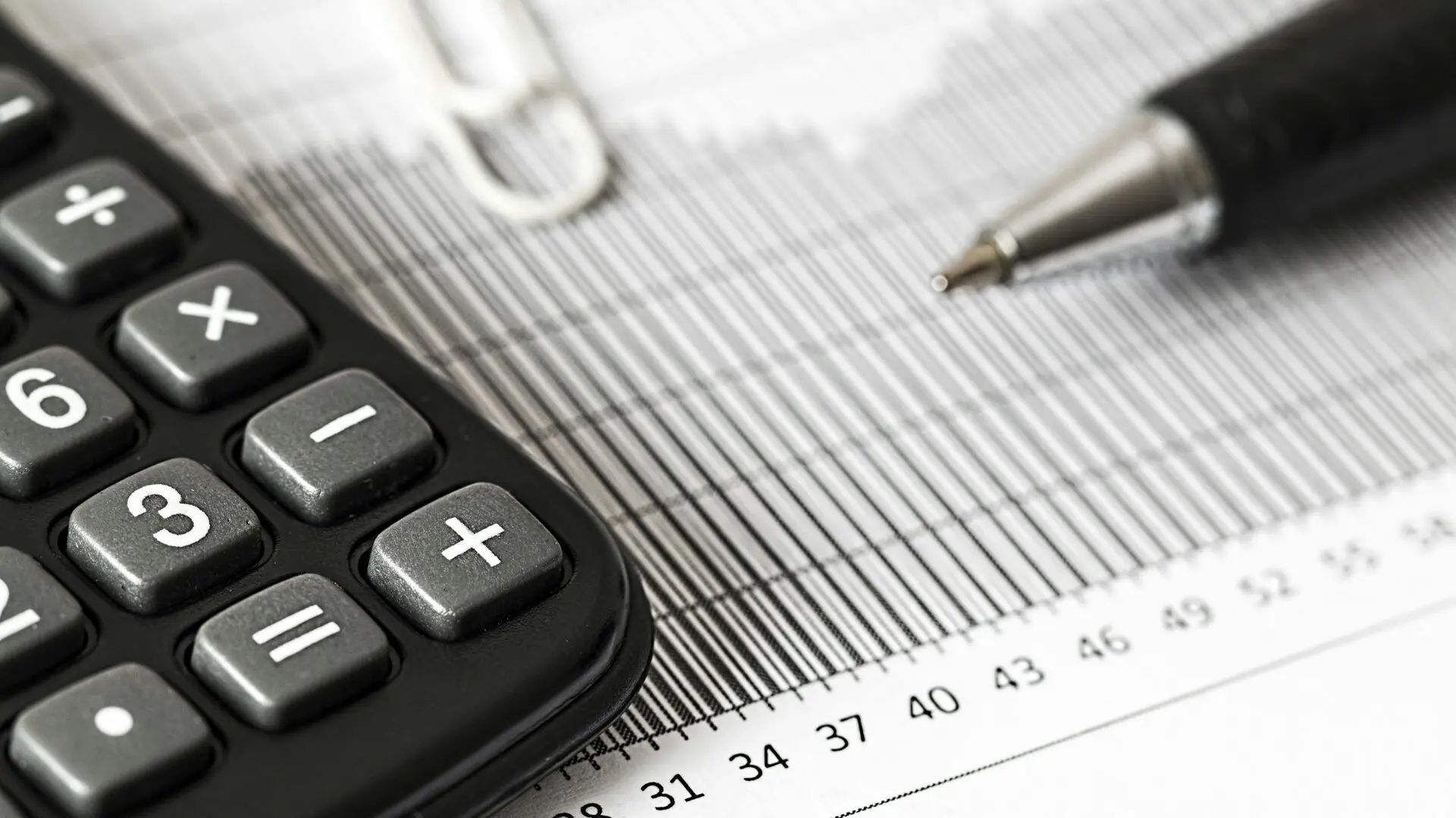 A close-up of a calculator and pen resting on a financial bar chart or tax document.