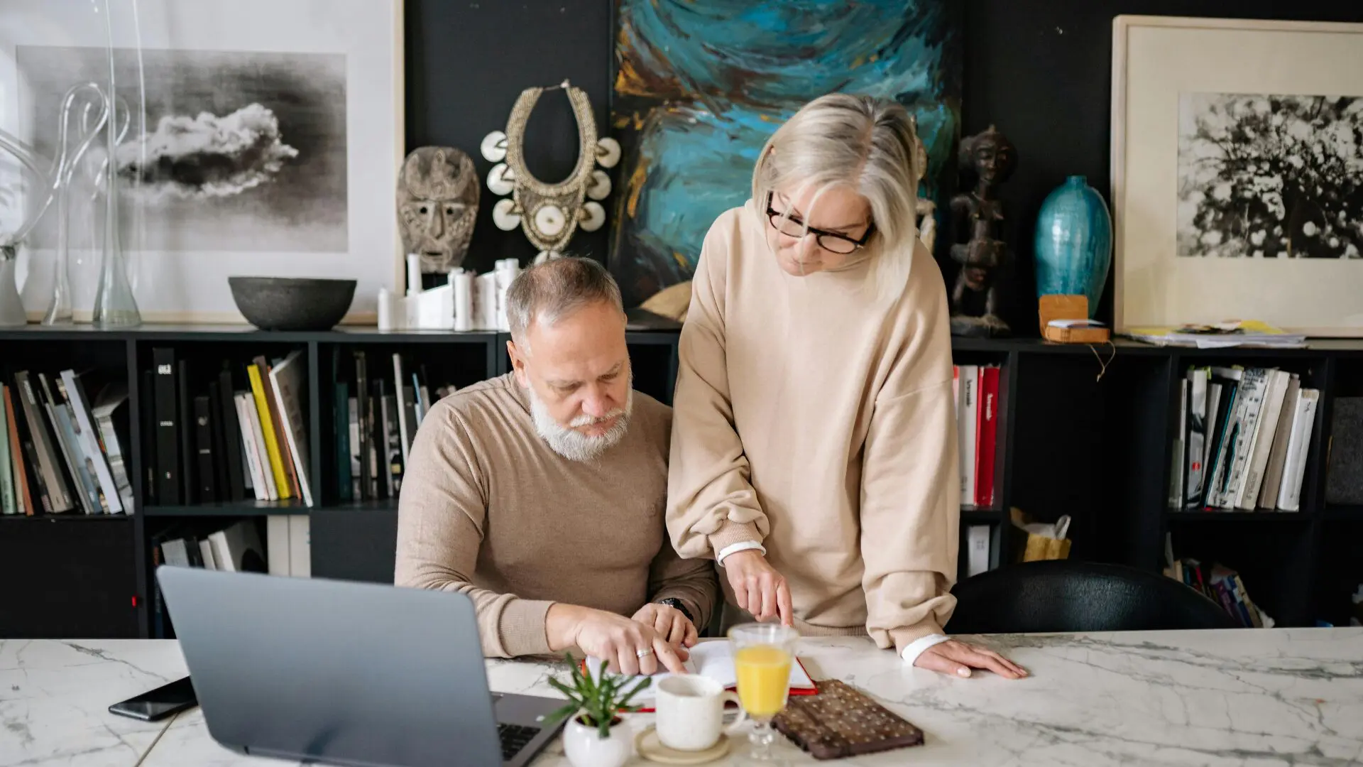 An elderly couple reviewing papers and using a laptop together in a living room, highlighting essential tax breaks for seniors.