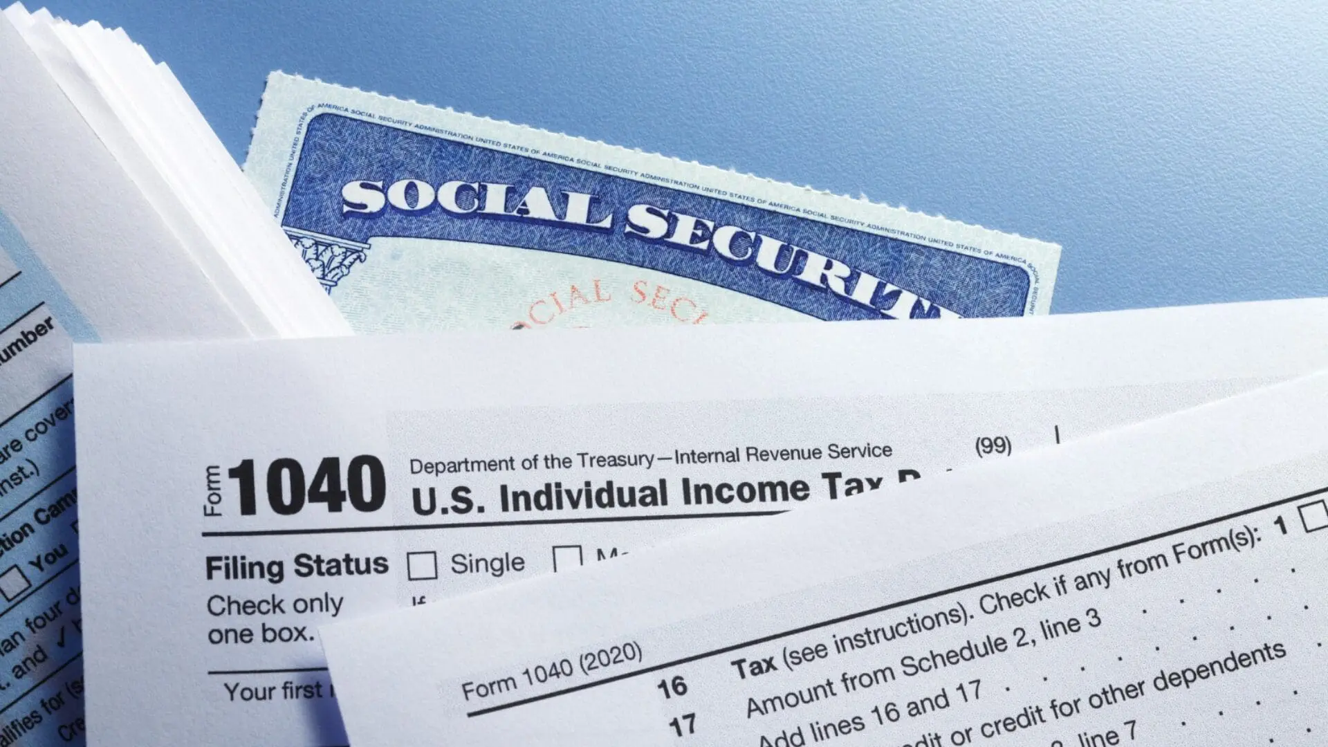 Close-up shot of an IRS Form 1040 U.S. Individual Income Tax Return document layered over a blue United States Social Security card against a light blue background.
