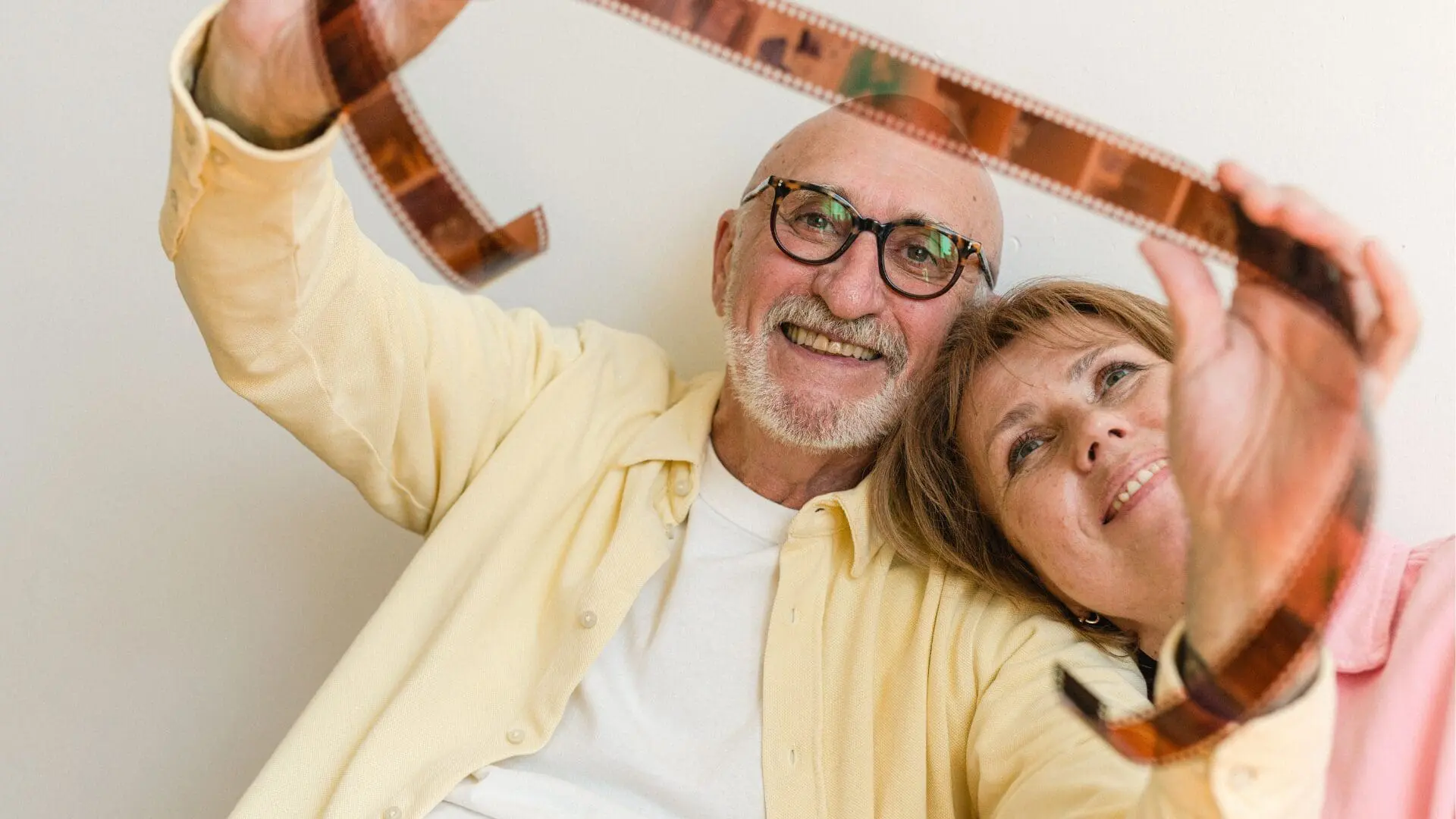A smiling, senior couple over 60 looking up through a strip of developed film negative, symbolizing reflection, letting go of the past, and embracing change.
