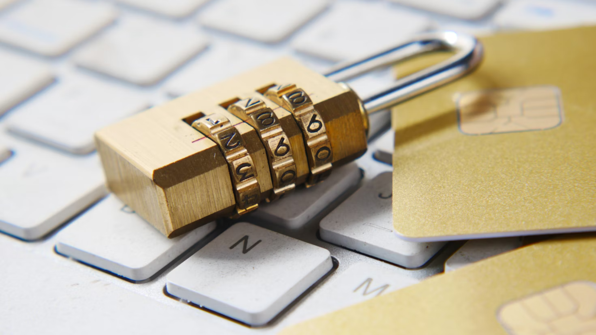 A combination padlock sitting on a computer keyboard with a credit card visible.