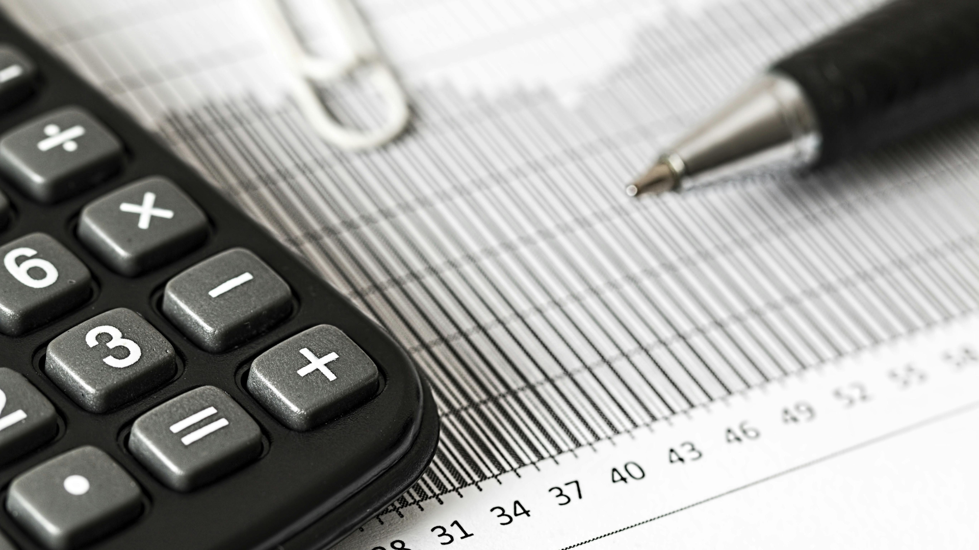 A close-up of a calculator and pen resting on a financial bar chart or tax document.