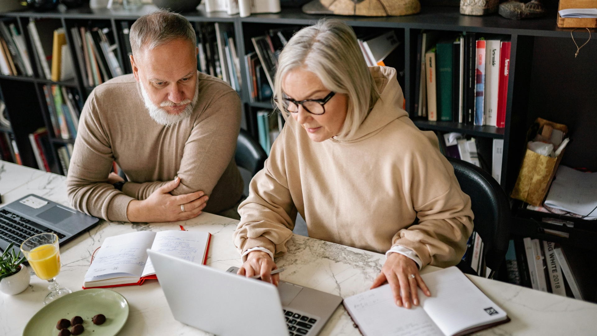 A senior couple, a man and a woman, looking at a laptop and documents on a white table.